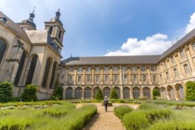Une personne marche devant l'Abbaye des Prémontrés depuis les jardins. On voit l'arrière de l'abbaye en arrière-plan.