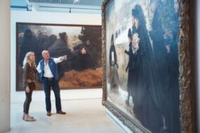 Un couple au musée des Beaux Arts de Nancy devant un tableau. L'homme montre à sa femme une oeuvre avec son doigt.